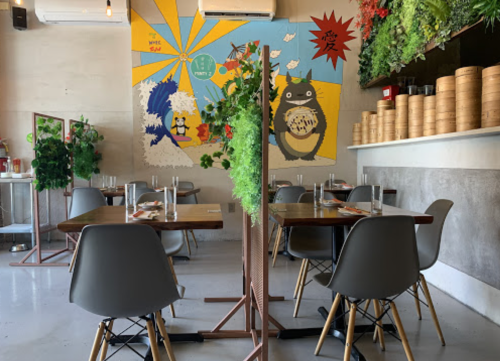 A cozy restaurant interior with wooden tables, modern chairs, and a colorful mural featuring a character and greenery.
