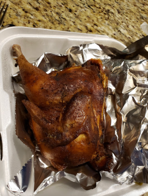 A roasted chicken leg resting on aluminum foil in a takeout container.