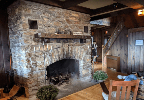 Cozy stone fireplace in a rustic room with wooden accents and a staircase in the background.