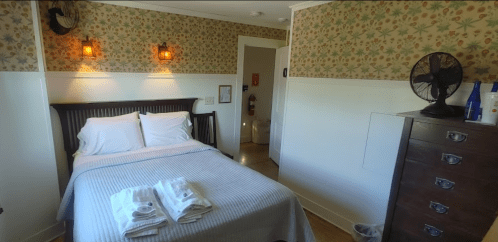 Cozy bedroom with a double bed, floral wallpaper, and a dresser, featuring fresh towels on the bed.