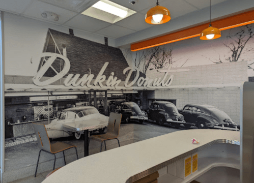A retro Dunkin' Donuts mural featuring classic cars, with a modern counter and pendant lights in the foreground.
