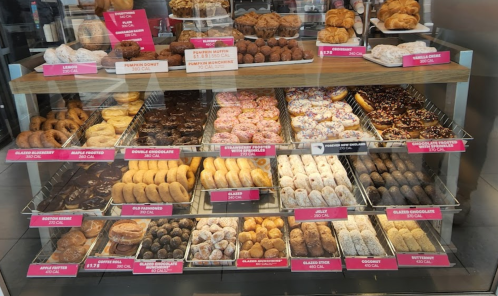 A display case filled with various donuts and pastries, labeled with prices and calorie counts.