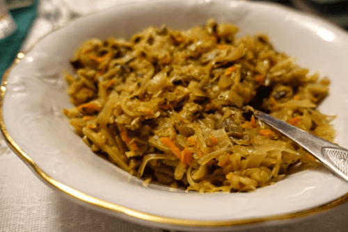 A close-up of a bowl of cooked cabbage and noodles, garnished with carrots, served with a silver spoon.