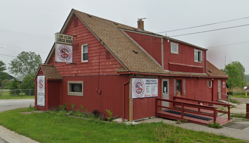 A red wooden building with a sloped roof, featuring signs for "The Olde Cheese House" and a ramp in front.
