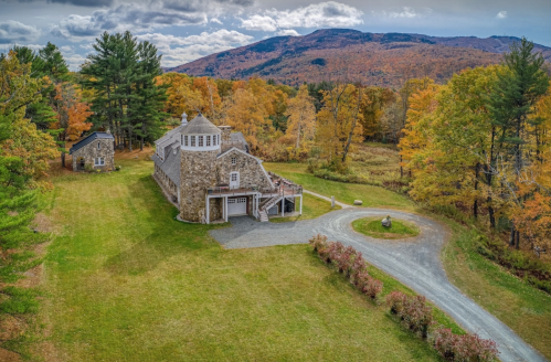 A scenic view of a stone building surrounded by colorful autumn trees and mountains in the background.