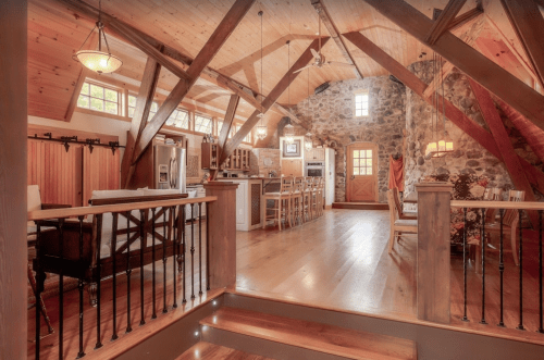 A spacious, rustic kitchen with wooden beams, stone walls, and a dining area featuring a large table and chairs.