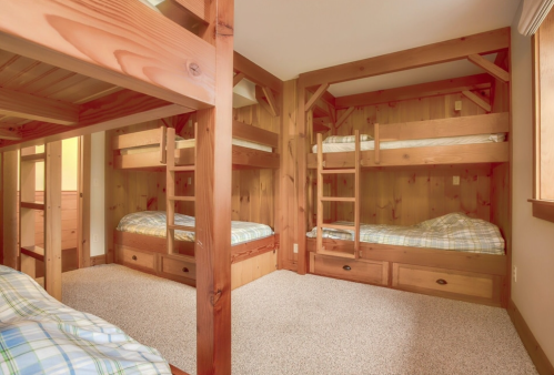 Cozy room with two sets of wooden bunk beds and plaid bedding, featuring warm wood paneling and carpeted floor.