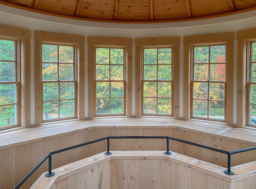 Interior view of a circular room with large windows showcasing colorful autumn foliage outside.