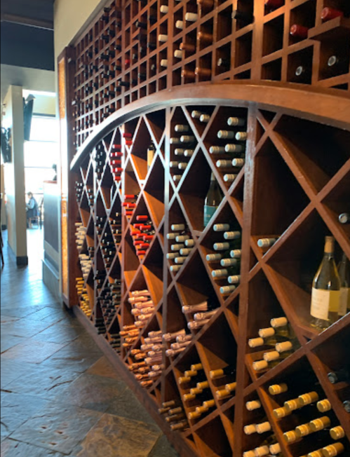A wooden wine rack displaying various bottles of wine in a restaurant setting.