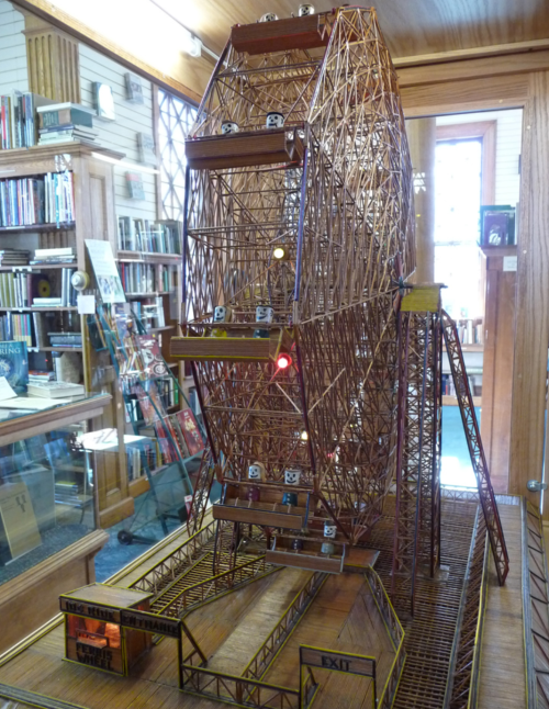 A detailed model of a Ferris wheel displayed in a library, showcasing intricate wooden construction and lights.