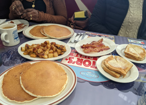 A table set with pancakes, bacon, toast, and home fries, alongside cups of coffee.