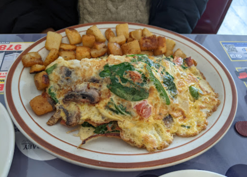 A plate of a vegetable omelette with spinach, tomatoes, and mushrooms, served with golden-brown potato cubes.