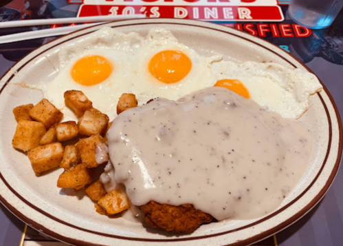 A plate of breakfast featuring two sunny-side-up eggs, chicken fried steak with gravy, and seasoned potato cubes.