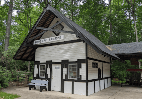 Historic train station building with a black and white exterior, surrounded by lush green trees.