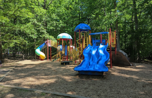 Colorful playground with slides and climbing structures, surrounded by trees and wood chips.
