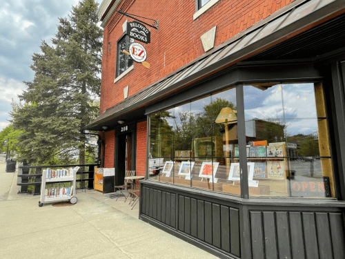 A cozy bookstore with large windows displaying books, located on a brick building with a sign that says "Open."