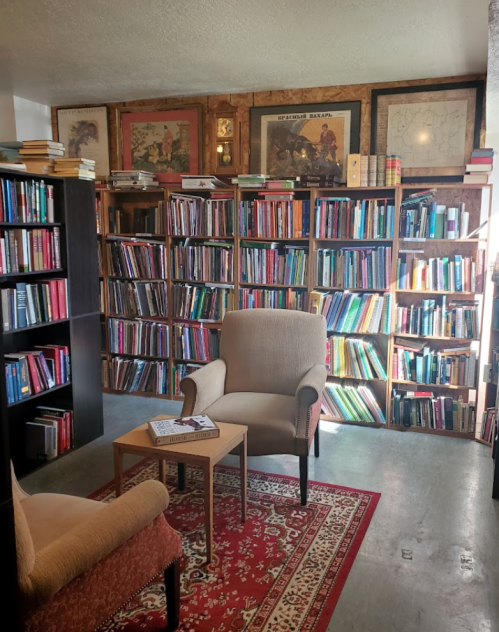 Cozy reading nook with two chairs, a small table, and shelves filled with colorful books in a warmly lit room.