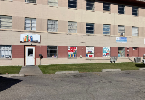 Exterior of a building with a sign for a community center, featuring colorful window displays and a grassy area.