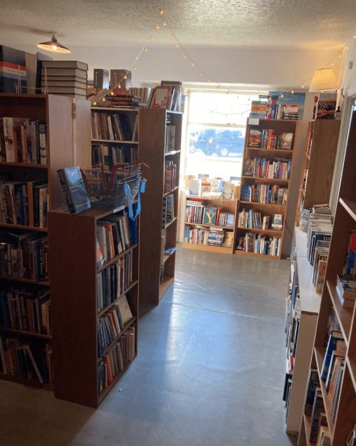 A cozy bookstore aisle lined with wooden shelves filled with books, illuminated by soft lighting and string lights.