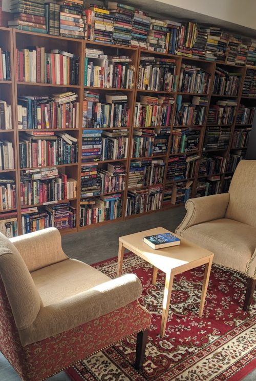 Cozy reading nook with two chairs, a small table, and a wall of bookshelves filled with books.