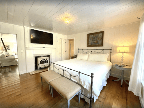 Cozy bedroom with a large bed, a TV, a decorative painting, and a bench, featuring white walls and wooden floors.