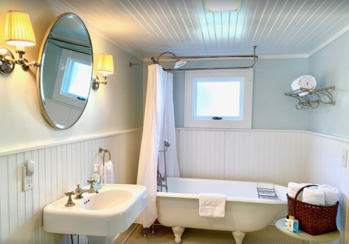 Bright bathroom featuring a clawfoot tub, sink, mirror, and white towels on a shelf. Soft lighting enhances the decor.