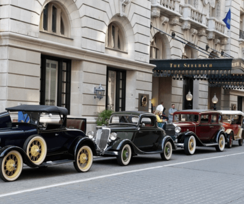 A row of vintage cars parked outside The Seelbach hotel, showcasing classic designs and colors on a city street.