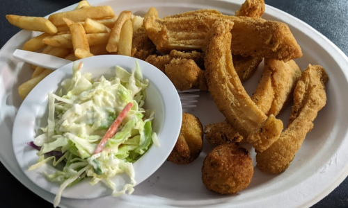 A plate of fried food featuring crispy chicken, hushpuppies, fries, and a side of coleslaw.