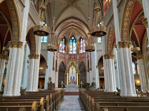 Interior of a grand church featuring tall arches, stained glass windows, and wooden pews.