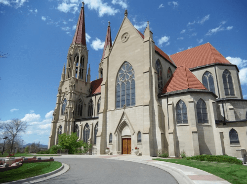 A tall, ornate church with spires and stained glass windows, set against a blue sky with scattered clouds.
