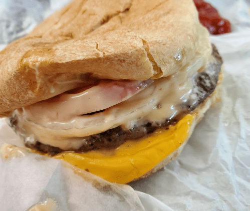 A close-up of a sandwich with a beef patty, melted cheese, and a fried egg, served on a soft bun.