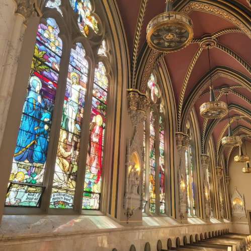 Stained glass windows in a grand, ornate hall with intricate architectural details and soft lighting.