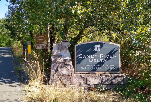 Sign for Sandy River Delta, Columbia River Gorge National Scenic Area, surrounded by trees and a pathway.