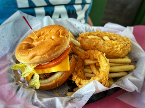 A burger with lettuce, tomato, and cheese, served with fries and onion rings on a paper-lined plate.