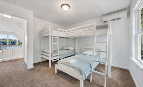 Bright bedroom with a bunk bed and a single bed, featuring large windows and a view of nature.