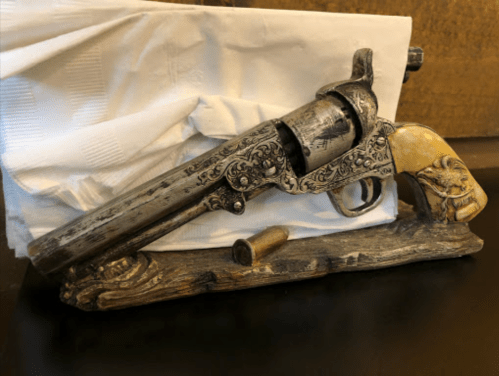 A decorative revolver with intricate designs, resting on a wooden base, alongside a bullet and white paper.