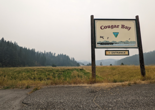 Sign for Cougar Bay entrance with a grassy field and smoky mountains in the background.