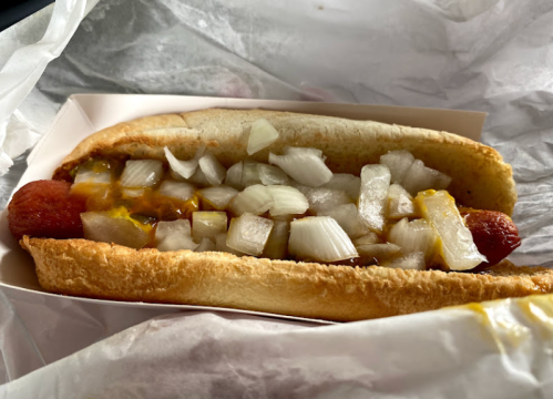 A hot dog in a bun topped with diced onions and mustard, served in a paper wrapper.
