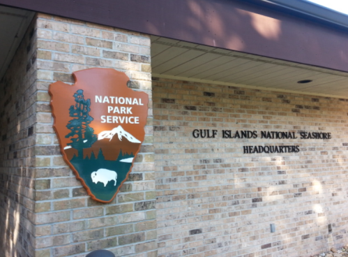 Sign for Gulf Islands National Seashore Headquarters featuring the National Park Service emblem on a brick wall.