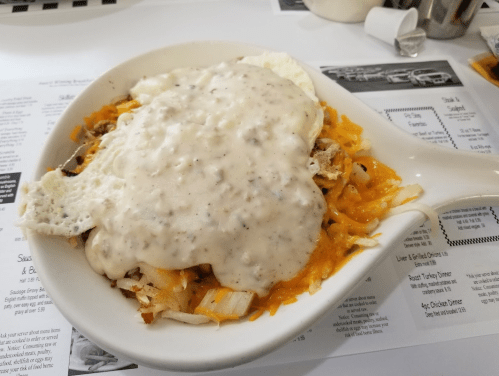 A dish featuring hash browns topped with cheese, sausage gravy, and a fried egg, served in a white bowl.