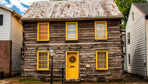 A rustic log cabin with a weathered roof, bright yellow windows, and a welcoming front door.