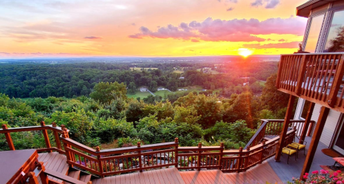 A scenic view of a sunset over a lush landscape, with wooden stairs leading down from a house.