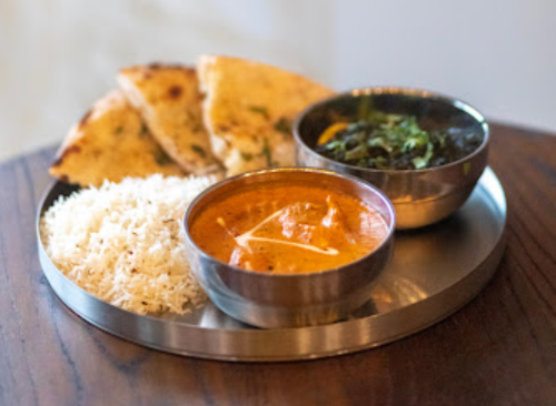 A metal plate with rice, curry, sautéed greens, and naan bread arranged neatly.