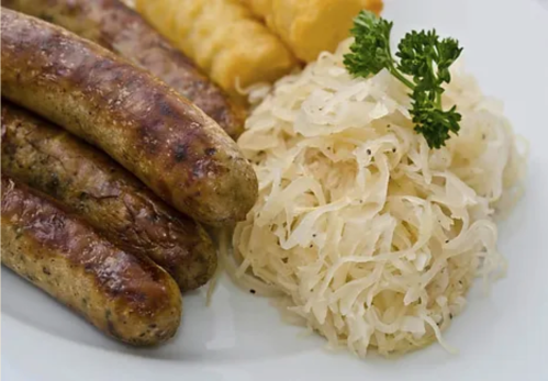Grilled sausages served with sauerkraut and a side of corn on a white plate, garnished with parsley.