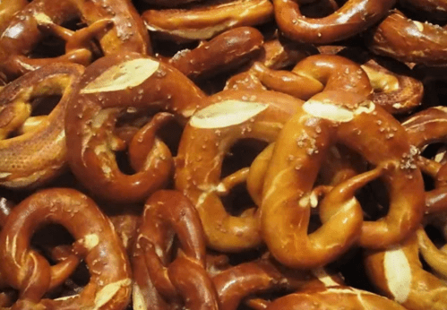 A close-up of a pile of golden-brown pretzels, some sprinkled with coarse salt and others with almond slices.