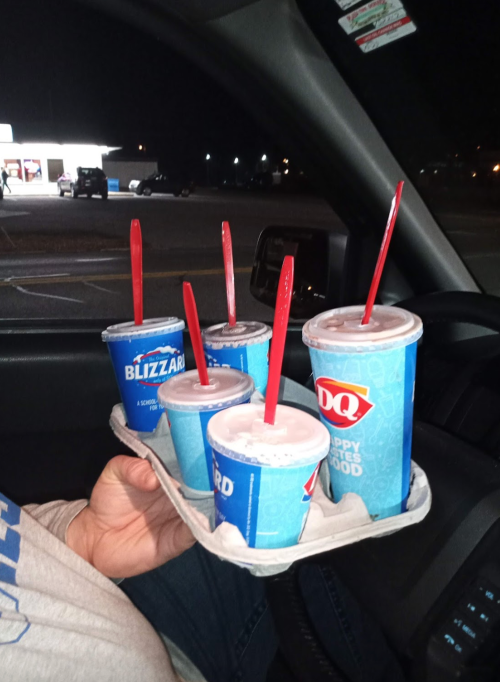 A person holds a tray with four Dairy Queen drinks, including Blizzards, inside a car at night.