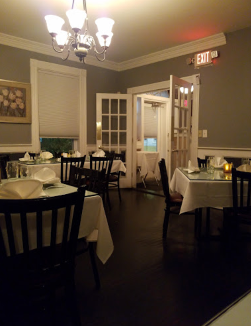 Cozy restaurant interior with tables set for dining, a chandelier, and an exit door in the background.
