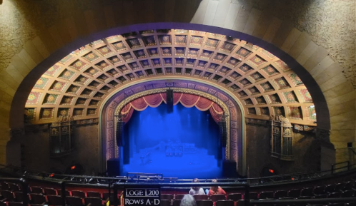 Interior of a theater with an ornate ceiling, empty seats, and a stage illuminated in blue light.