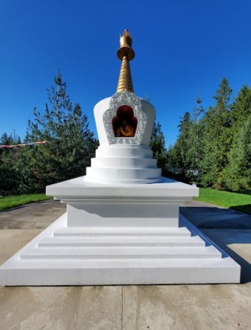 A white stupa with a golden spire, surrounded by green trees and a clear blue sky.