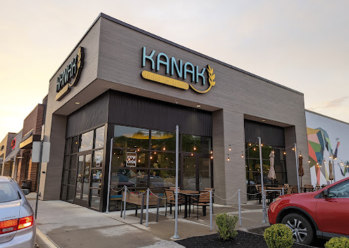 Exterior of Kanak restaurant with modern design, large windows, and outdoor seating area, set against a colorful mural.